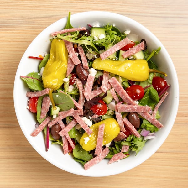 Overhead view of a vibrant salad with salami, peppers, olives, tomatoes, and feta cheese.