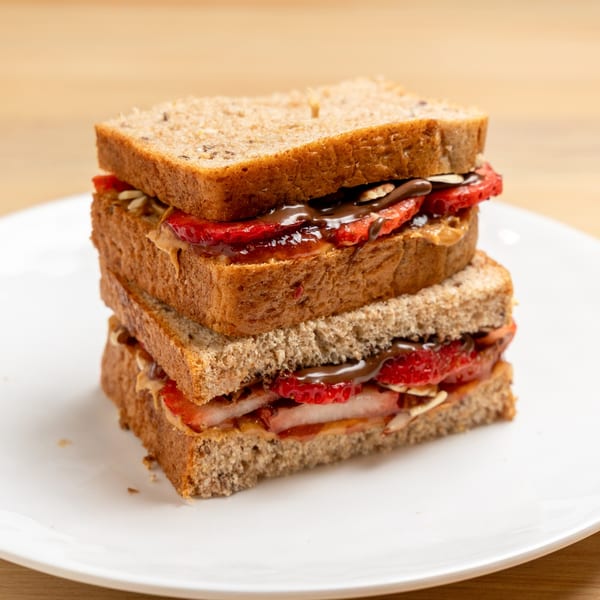 Two stacked sandwiches on whole wheat bread with peanut butter, strawberries, and chocolate drizzle.