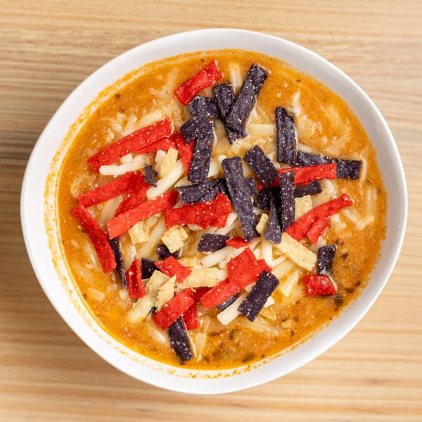 Overhead view of a bowl of tortilla soup with red, blue, and white tortilla strips.