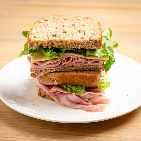 Double-decker ham and cheese sandwich on whole wheat bread with lettuce, on a white plate.