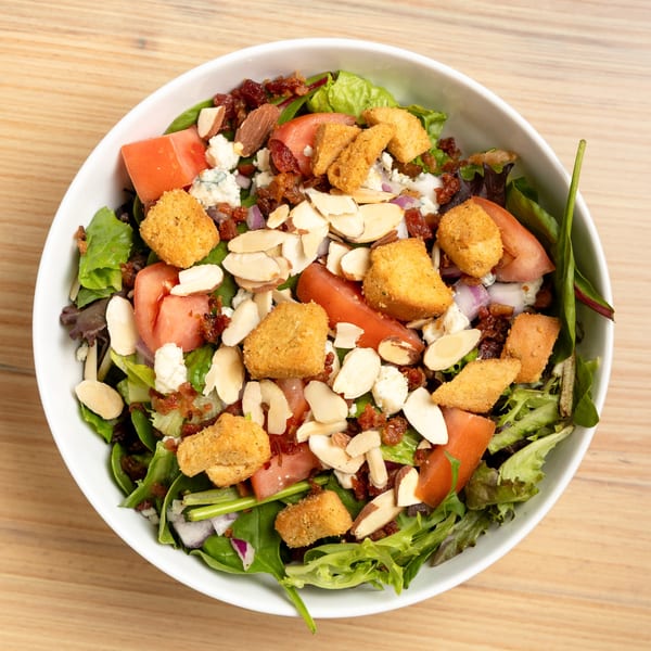 Overhead view of a salad with greens, tomatoes, almonds, bacon bits, and fried goat cheese.