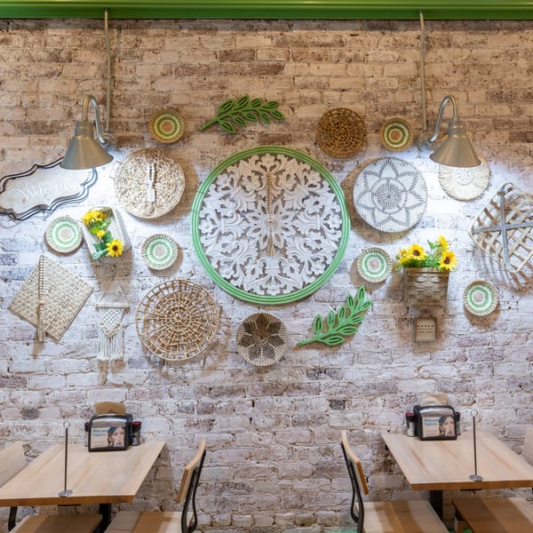 A rustic restaurant interior with a white brick wall decorated with woven baskets and green accents.