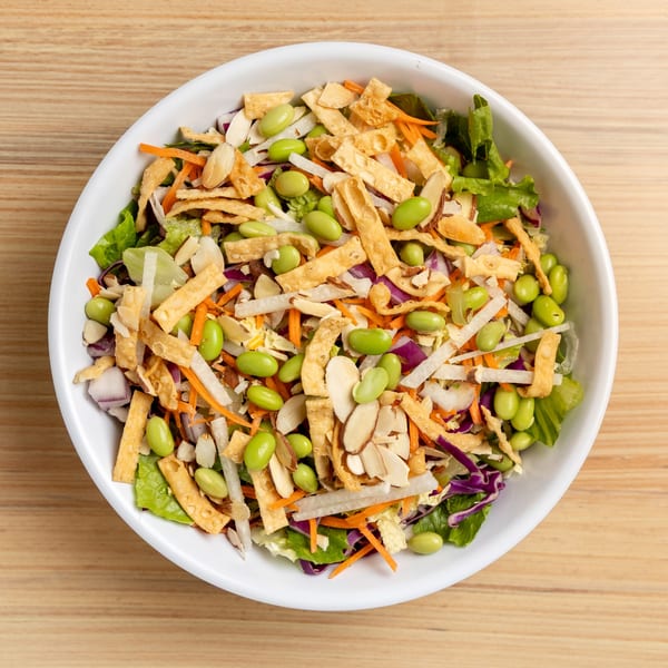 Overhead view of an Asian salad with lettuce, edamame, carrots, almonds, and crispy wonton strips.