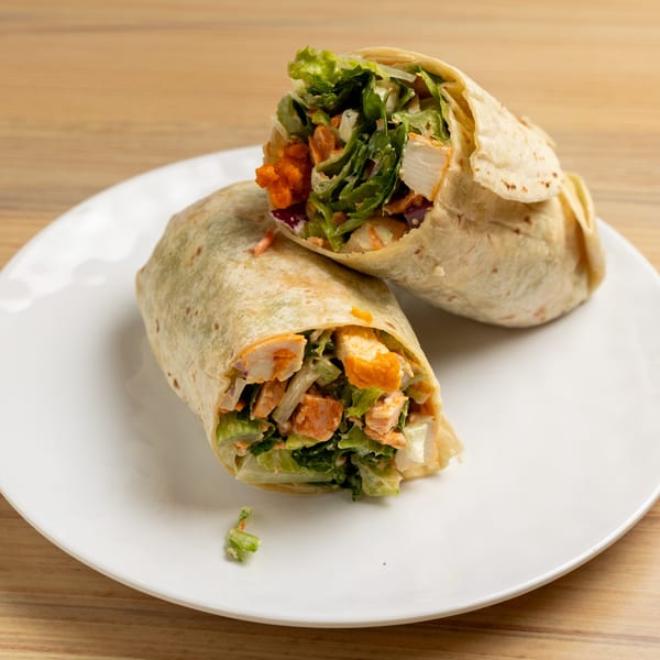 Two halves of a buffalo chicken wrap, filled with lettuce and chicken, on a white plate.
