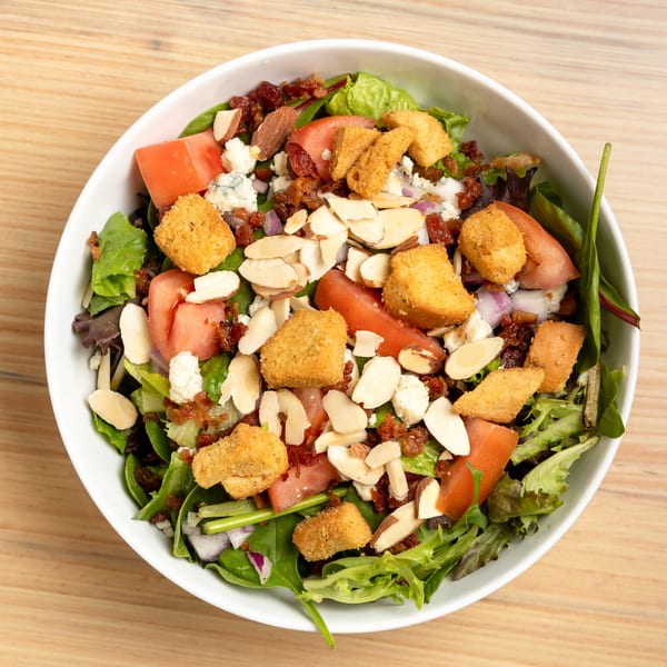 Overhead view of a salad with greens, tomatoes, almonds, bacon bits, blue cheese, and croutons.