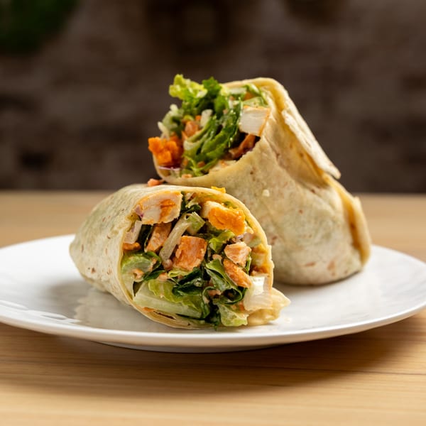 Two buffalo chicken wraps, filled with lettuce and chicken, on a white plate.