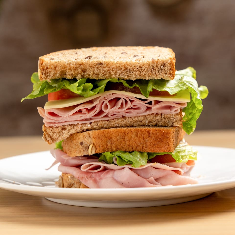 A tall, stacked ham and cheese sandwich with lettuce and tomato on whole wheat bread.