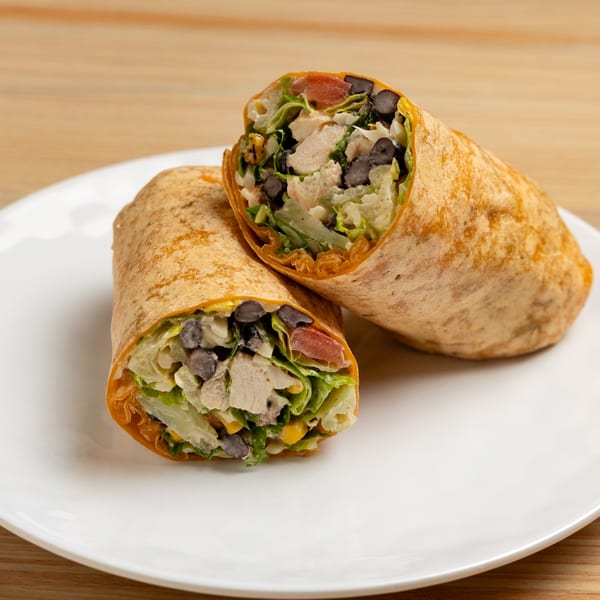 Two halves of a chicken and black bean wrap with lettuce, corn, and tomato on a white plate.