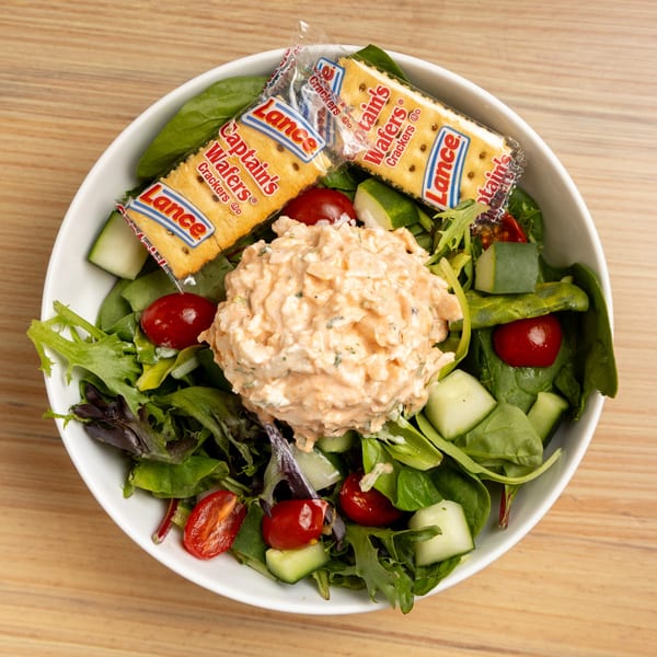 A salad with chicken salad, mixed greens, cherry tomatoes, cucumbers, and Lance crackers.