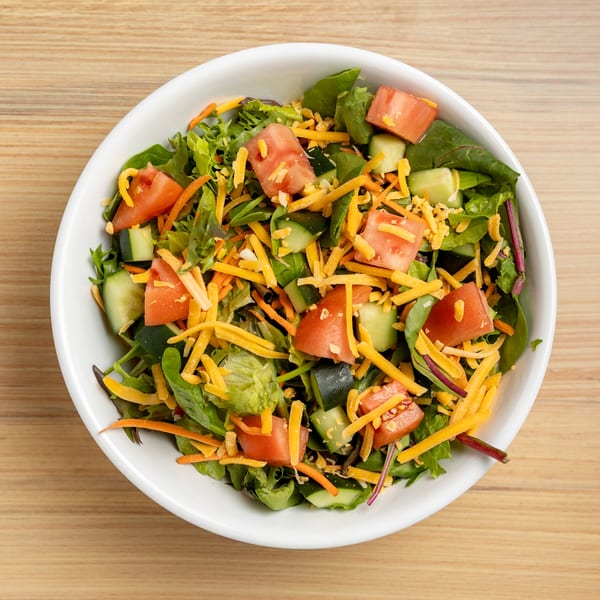 A fresh garden salad with mixed greens, diced tomatoes, cucumbers, and shredded cheddar cheese.