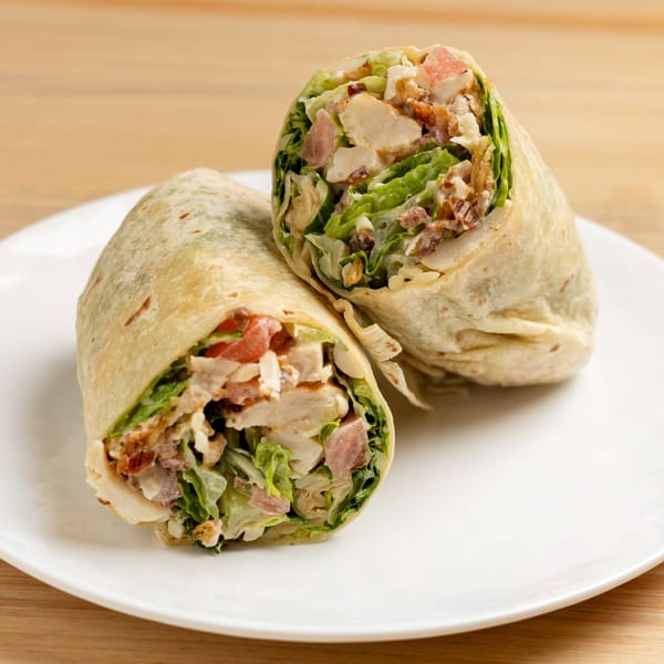 Two halves of a chicken Caesar wrap, filled with lettuce, chicken, bacon, and dressing.