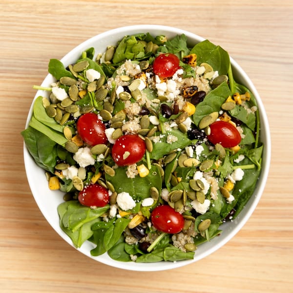 Overhead view of a vibrant salad with spinach, quinoa, cherry tomatoes, feta, pumpkin seeds, and corn.